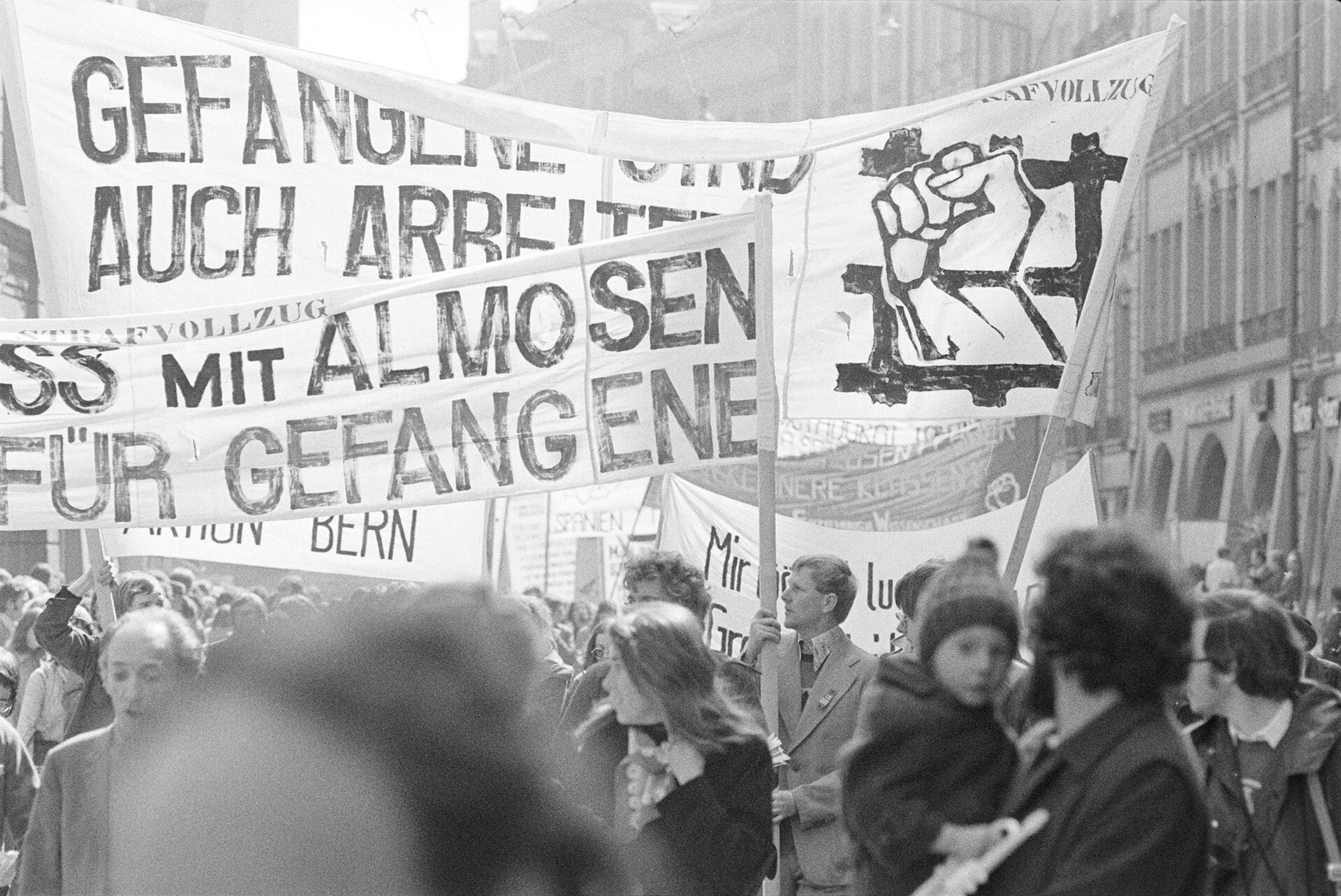 Fotografia in bianco e nero della manifestazione del 1° maggio 1976 a Berna. Diversi manifestanti con striscioni contro il sistema penitenziario.