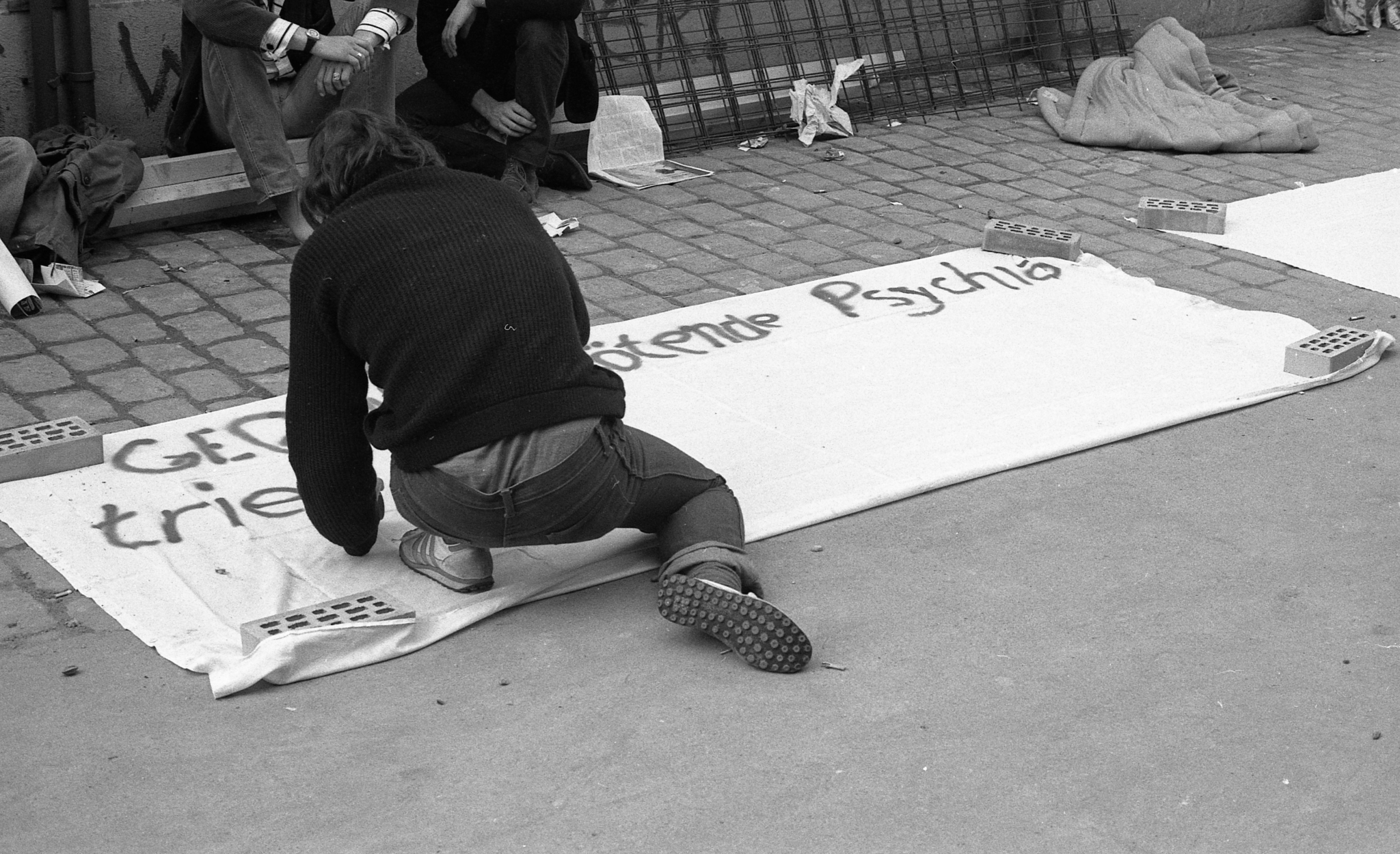 Fotografia in bianco e nero di una persona all'AJZ (Autonomes Jugendzentrum Zürich, Centro giovanile autonomo di Zurigo) che dipinge uno striscione con lo slogan «Contro la psichiatria che uccide». La foto è stata scattata il 12 luglio 1980 e documenta il movimento giovanile degli anni '80.