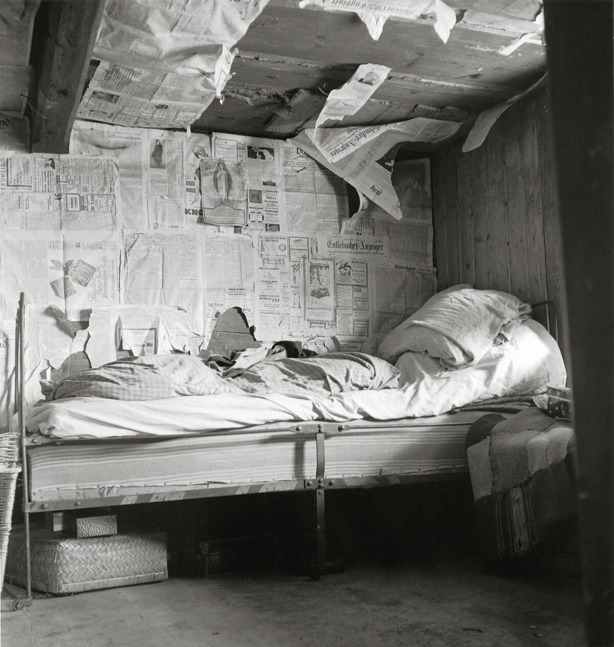 Fotografia in bianco e nero. Letto in una stanza isolata con vecchi giornali. L'immagine mostra le condizioni abitative povere a Flühli nell'Entlebuch (LU), 1947.
